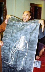 Jisu Sunim holding up a rubbing of Bodhidharma which has just been presented to him by Shi Yanzi. Photo © Gerda Chapuis