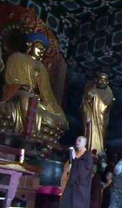 Chinese monk walking passed Buddha rupa. Possibly a statue of bodhidharma on right.
